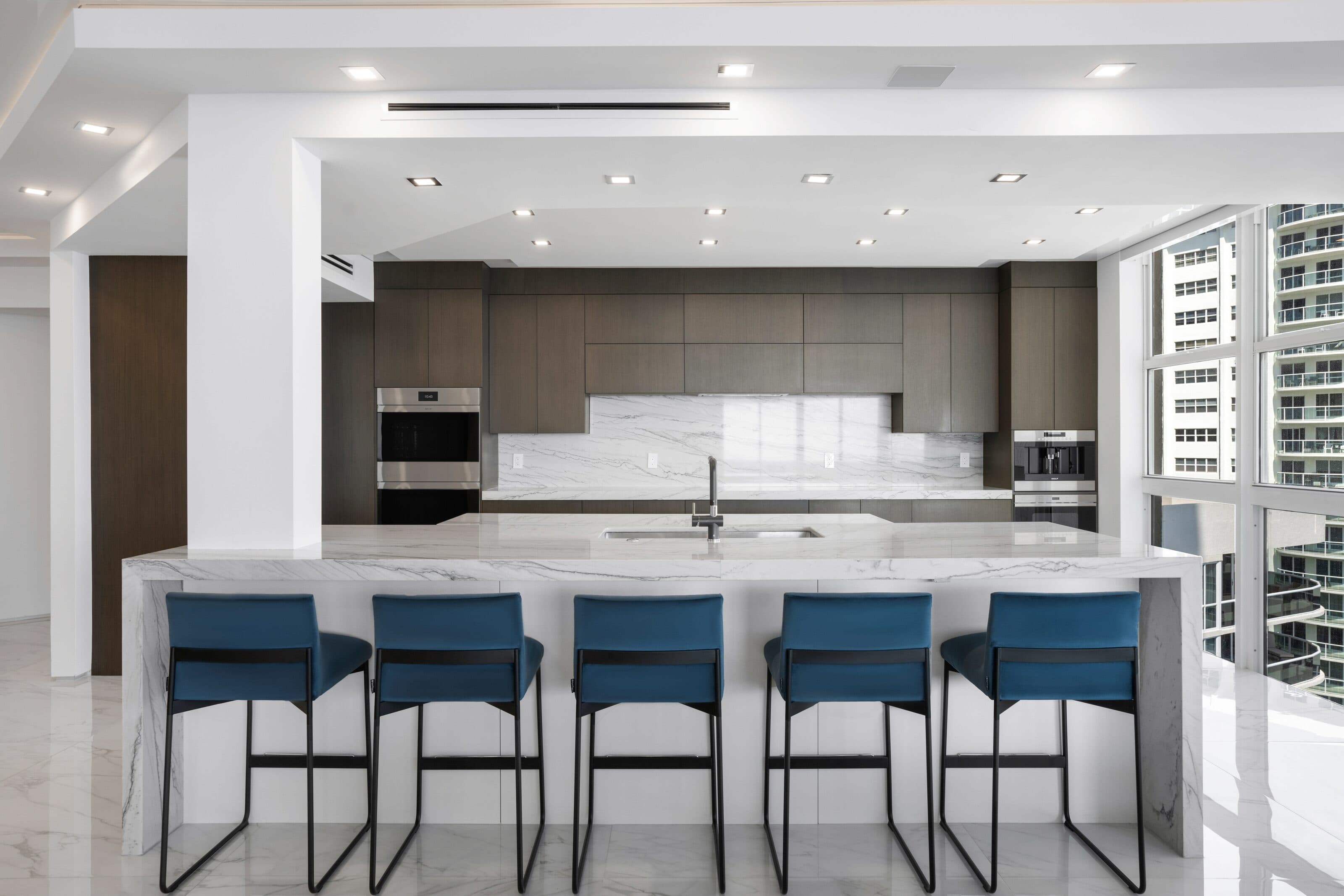 Stone City kitchen with a Giotta quartzite waterfall island, blue counter stools and dark wood cabinetry