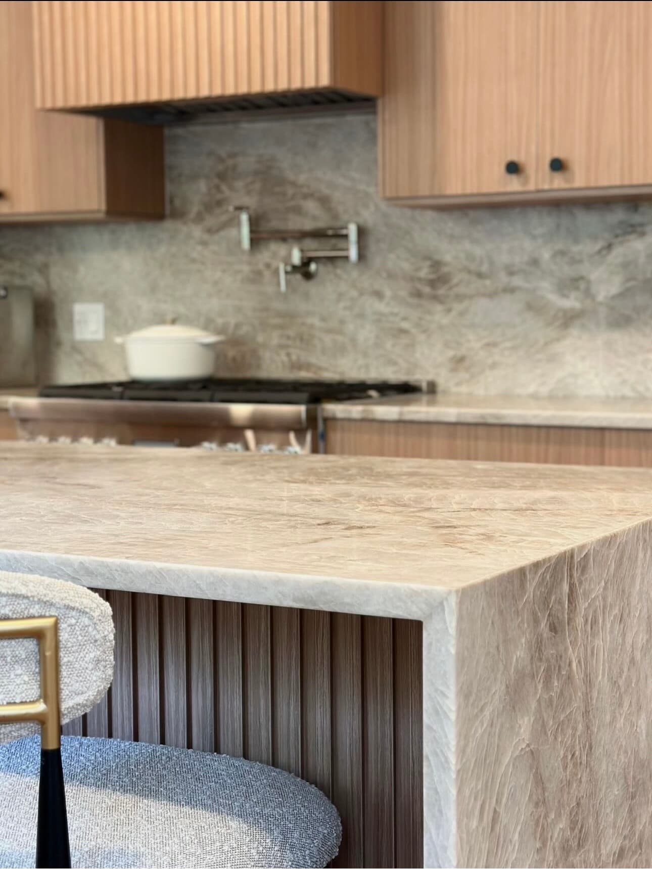 Close-up of the island’s stone waterfall edge, with fluted wood below and a stone backsplash behind