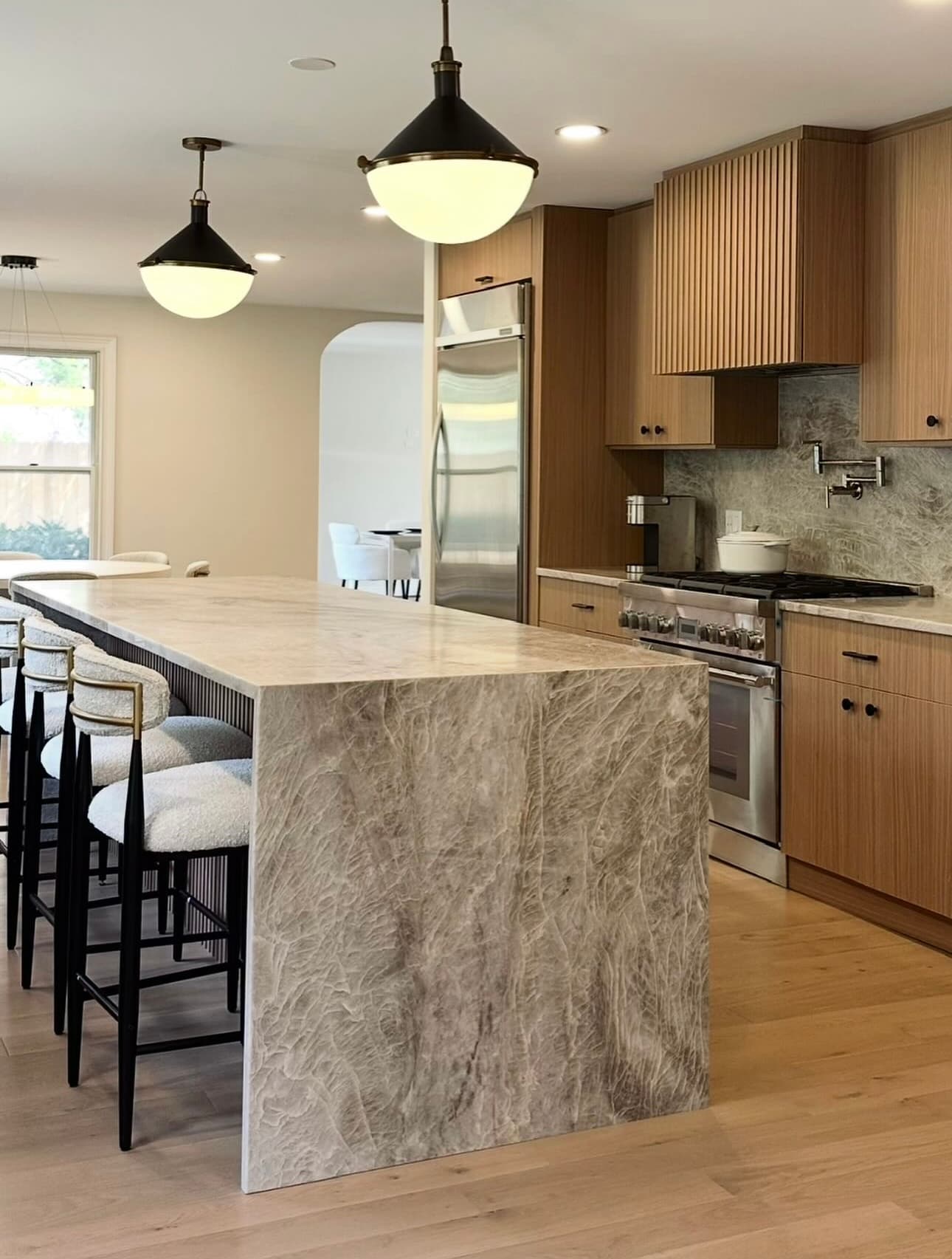 Kitchen with a stone waterfall island, globe pendant lights and warm wood cabinetry